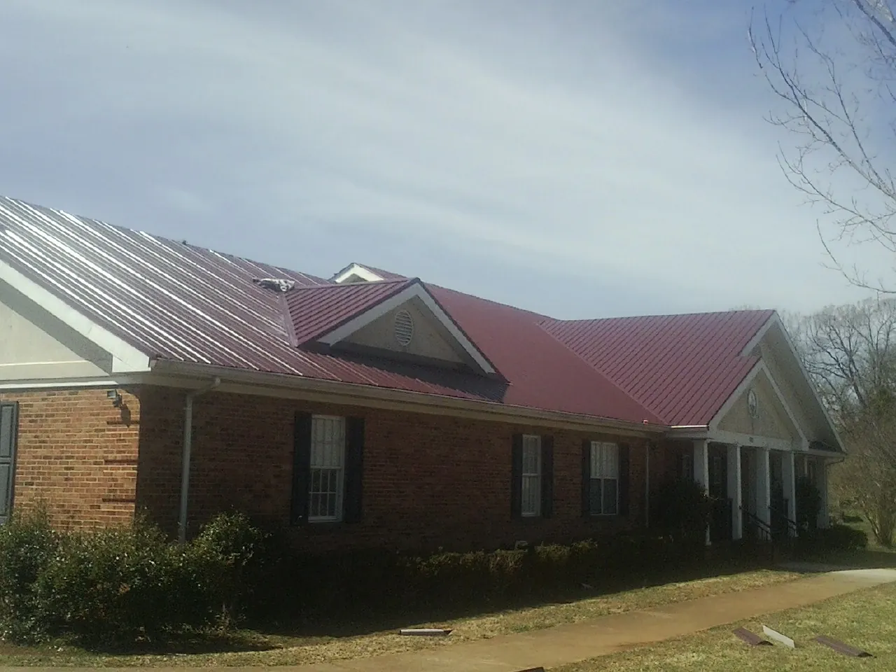 Red metal roof with gabled entries on a long brick building, from a Hail Damage Roof Repair job in Vinton