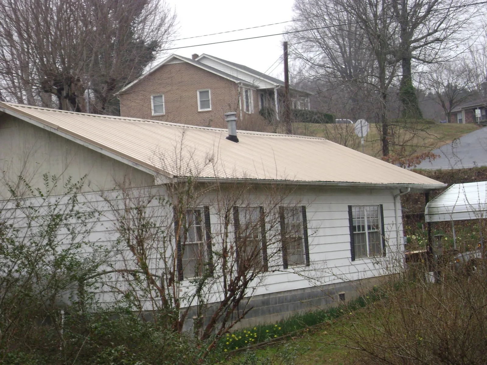 Tan metal roof on a white sided house set into a hillside — Commercial Roofing by Roofing Brothers in Vinton